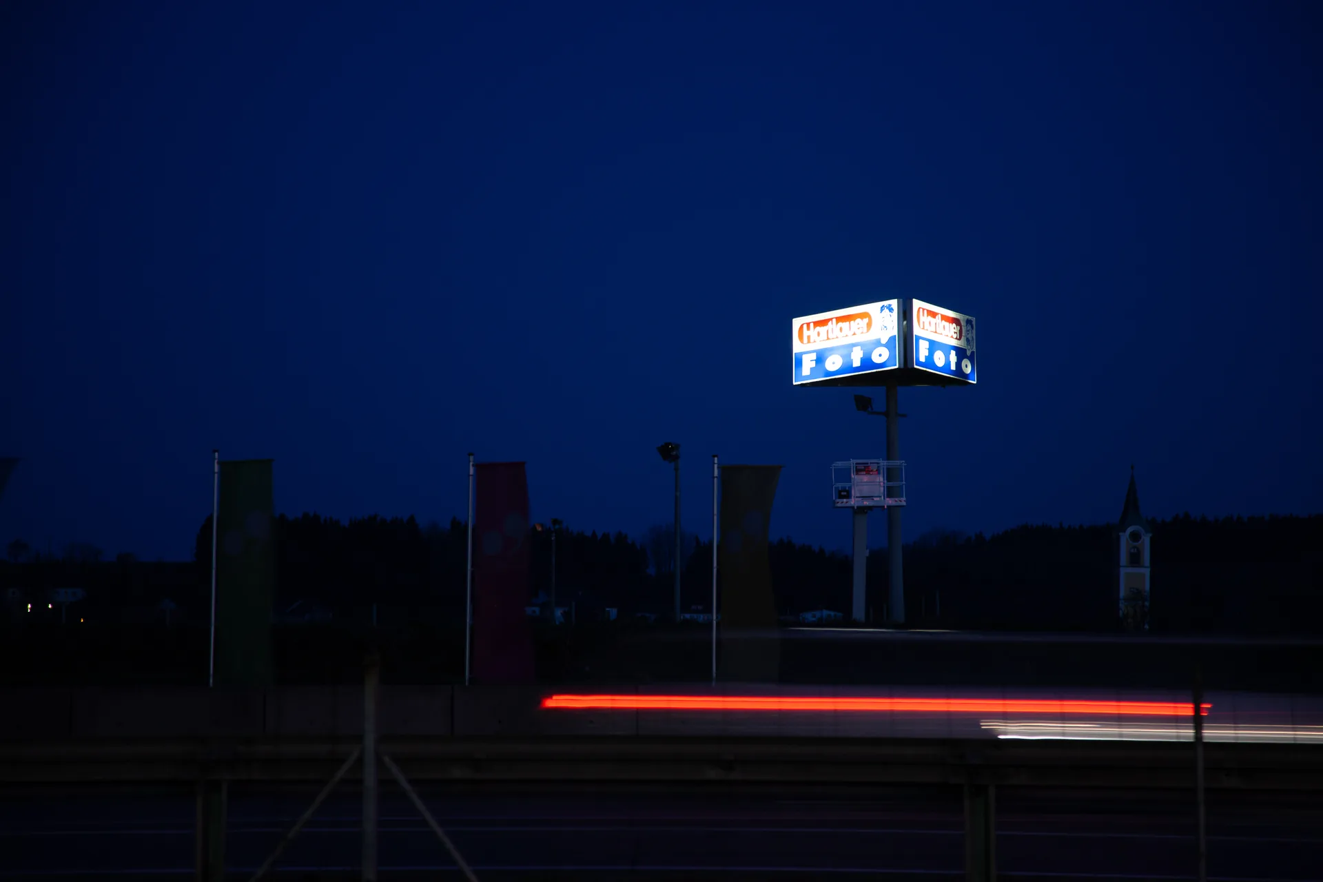 Lichtspur eines Autos vor einem leuchtenden Schild in der Dämmerung