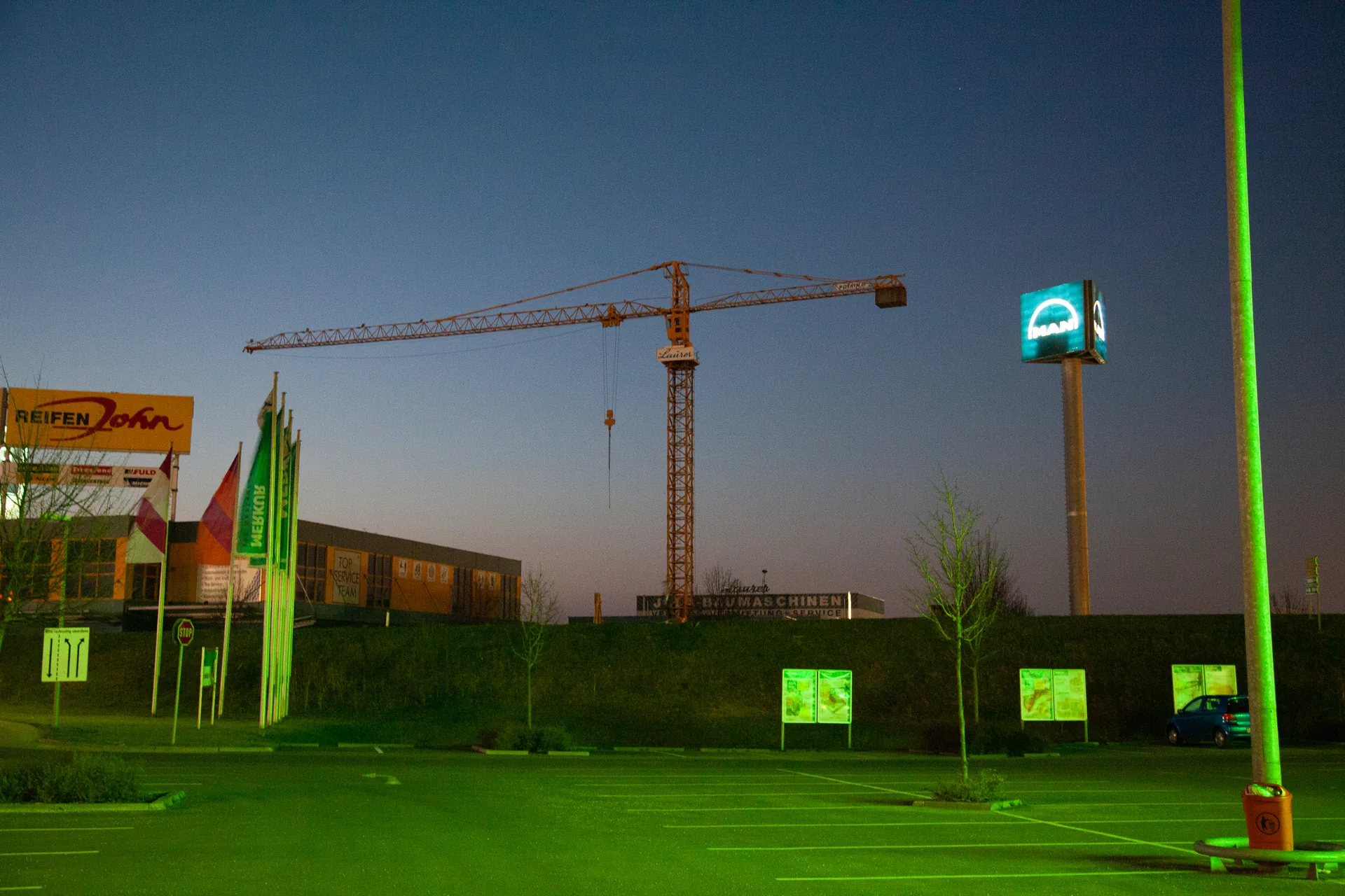 Baukran und grün beleuchteter Parkplatz am Abend