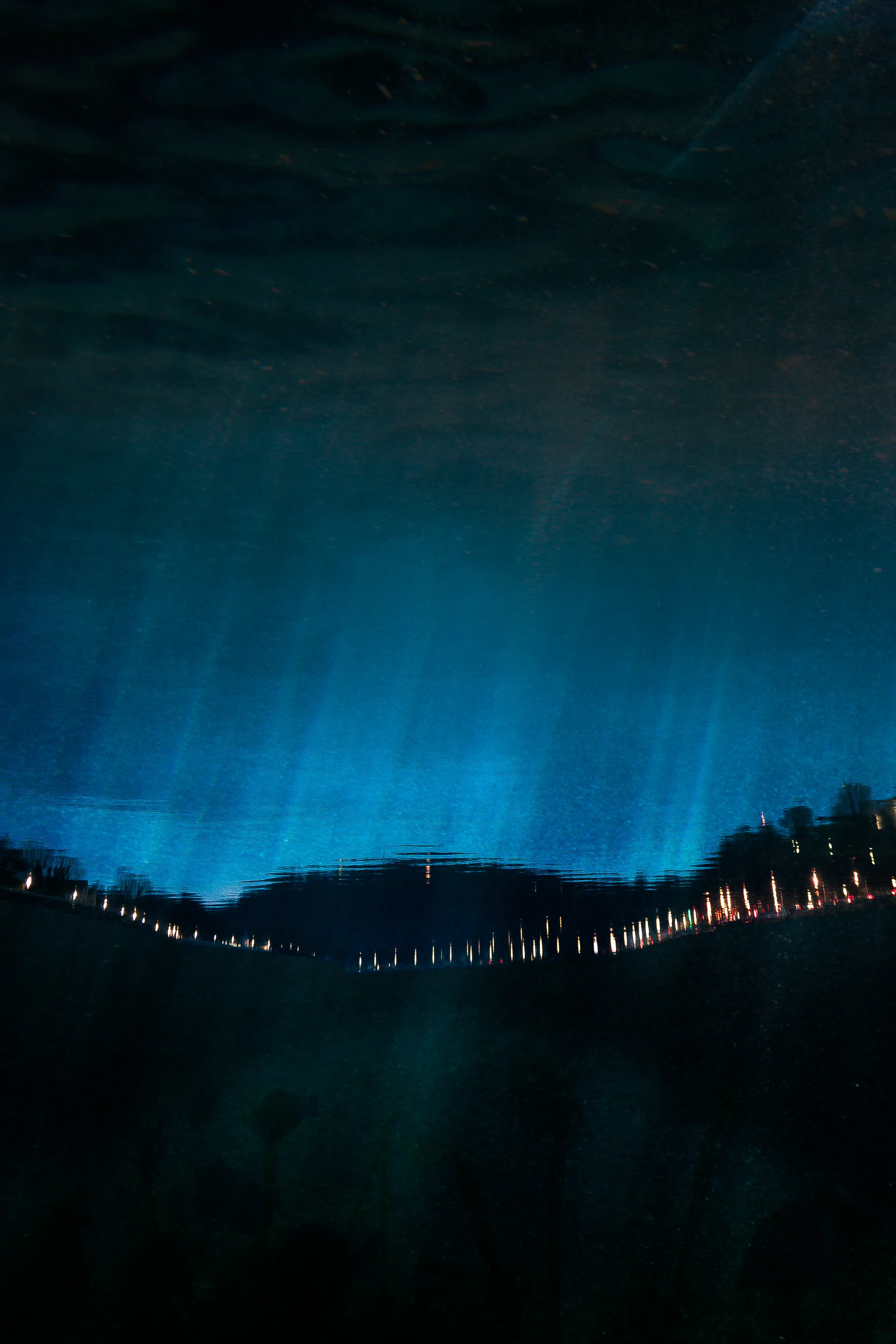 Dunkle Landschaft in Blau, Lichterkette am Horizont