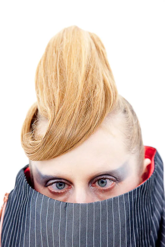 Person mit blonder Tolle, die Augen über einem hochgezogenen Kragen